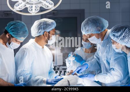 Pour l'oxygénation avant l'anesthésie générale. L'équipe chirurgien ciblée opérant dans une salle d'opération, filtre bleu Banque D'Images