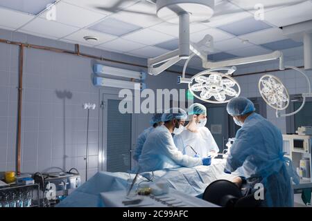 Chirurgien mâle holding instrument dans l'abdomen du patient. Les assistants, hommes et femmes de l'aider. Chirurgien indien d'effectuer la chirurgie laparoscopique dans operatin Banque D'Images