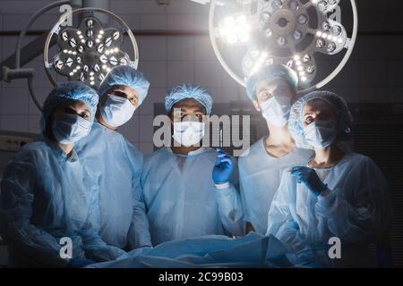 Concept hospitalier. Équipe de chirurgie regardant la caméra dans la salle d'opération d'une clinique d'hôpital pendant l'opération sur un patient en cas d'urgence Banque D'Images
