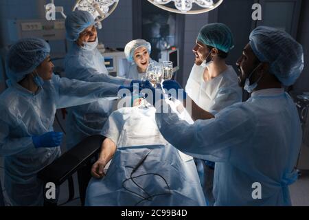 Se joindre à l'équipe de chirurgiens multiethnique mains ensemble avec des verres de jus de pomme, après le sauvetage d'encouragement patient en salle d'opération à l'hôpital. Banque D'Images