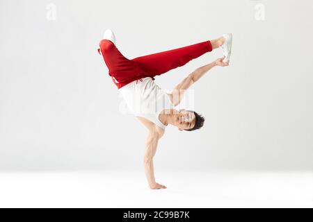 Jeune b-boy sportif debout d'une main tout en dansant la danse de pause et faisant le downrock isolé sur fond blanc de studio. Banque D'Images