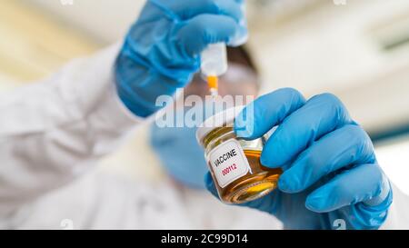 Chercheur en vêtements de protection en laboratoire. COVID-19 recherche sur les vaccins. Mains dans des gants bleus tenant une seringue et un flacon en verre avec du liquide jaune.