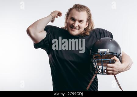 Beau joueur sportif américain de football tenant son casque dans les bras regardant la caméra avec une expression gaie et confiante posant sur la ba blanche Banque D'Images