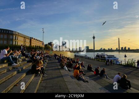 Personnes assises sur les marches de la terrasse du Rhin (Rheintreppe) à Burgplatz, le Rhin, et appréciant le coucher du soleil. Banque D'Images