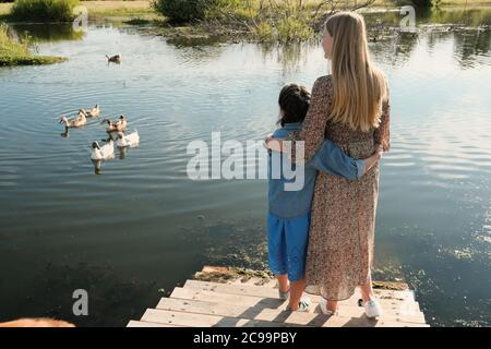 Vue arrière de la mère et de la fille s'embrassant en se tenant sur le pont et en regardant les cygnes sur la rivière à l'extérieur Banque D'Images