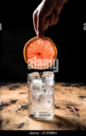 Recette de gin et de cocktail tonique, main tenant une tranche de pamplemousse sur un verre de High ball, table en bois, fond sombre Banque D'Images