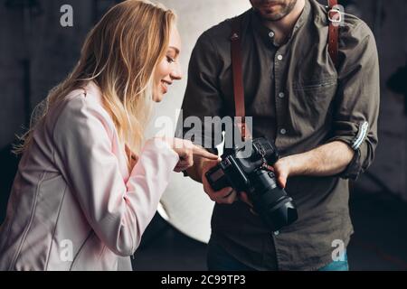 génial jolie fille pointant vers la photo tout en travaillant avec un photographe, fille gaie donnant des conseils pour le photographe au studio Banque D'Images