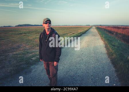 Un homme en lunettes de soleil avec un sac à dos va la route de gravier, vue d'automne Banque D'Images