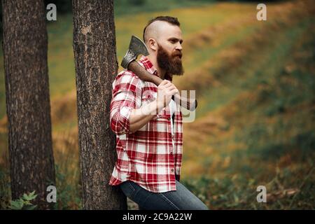 Mohawk barbu de bûcheron en forêt avec ax Banque D'Images