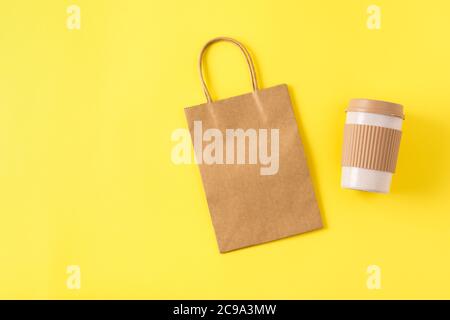 Maquette de sac de shopping en papier kraft avec poignées sur surface jaune, tasse à café portable réutilisable pour les voyages. Tasse à emporter avec bouchon anti-éclaboussures. Banque D'Images