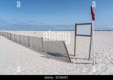 panneau blanc vierge sur la plage de sable blanc avec clôture de tempête et drapeau rouge Banque D'Images