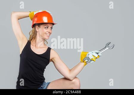 femme blonde dans un casque de protection et des gants, tenant une grande clé dans ses mains, pointe vers un espace vide. Banque D'Images