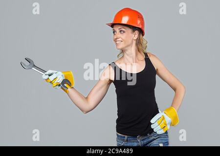 femme blonde dans un casque de protection et des gants, tenant une grande clé dans ses mains, pointe vers un espace vide. Banque D'Images