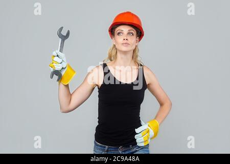 femme blonde dans un casque de protection et des gants, tenant une grande clé dans ses mains, pointe vers un espace vide. Banque D'Images