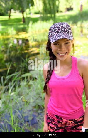 Joyeux sourire jeune fille asiatique en casquette sport et portrait d'activewear rose. Femme chinoise de race blanche multiraciale dans ses 20 ans en plein air Banque D'Images