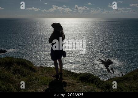 Fille avec de longs cheveux et chapeau debout sur une falaise à Cornwall avec vue sur la mer Banque D'Images