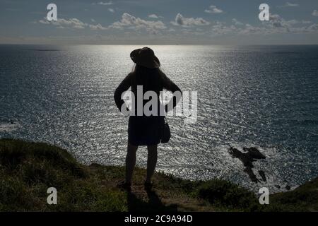 Fille avec de longs cheveux et chapeau debout sur une falaise à Cornwall avec vue sur la mer Banque D'Images