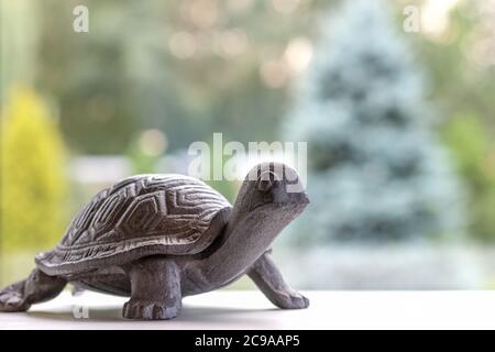 une petite tortue de fer brun sur une surface blanche près de la fenêtre devant le jardin un jour ensoleillé, il y a une forme de sapins, idée de vivre lentement, profiter du mode de vie de la campagne, animal artificiel Banque D'Images