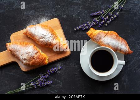 Tasse de café et croissants, bouquet de fleurs de lavande sur table noire, vue sur le dessus. Concept petit déjeuner. Banque D'Images