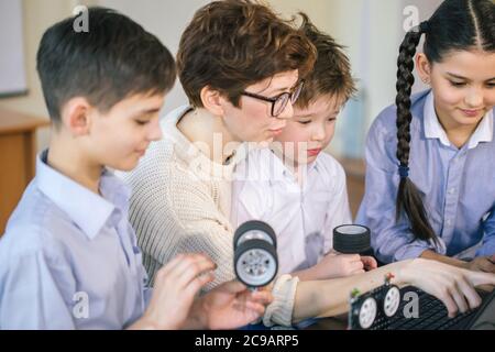 Curieux élèves ingénieux avec l'aide de leur enseignante sur un groupe de programmation du projet des ordinateurs portables à l'aide du robot sur classes parascolaires Banque D'Images