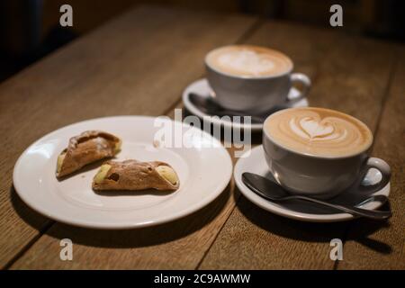 Deux cannoli sur une assiette et deux cafés debout sur une table en bois lavée dans un café. Banque D'Images