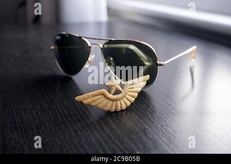 Badge de casquette d'ailes de pilote de couleur or et lunettes de soleil style aviateur sur un bureau en bois noir Banque D'Images