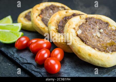 Délicieux plats libanais (arabes), de véritables sfihas sur une assiette en ardoise avec des tomates et des citrons. Banque D'Images
