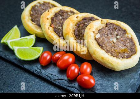 Délicieux plats libanais (arabes), de véritables sfihas sur une assiette en ardoise avec des tomates et des citrons. Banque D'Images