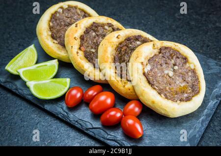 Délicieux plats libanais (arabes), de véritables sfihas sur une assiette en ardoise avec des tomates et des citrons. Banque D'Images
