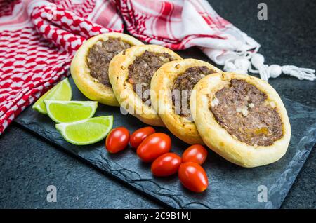 Délicieuse cuisine libanaise (arabe), véritables sfihas sur une plaque d'ardoise avec tomates et citrons à l'arrière-plan avec le keffiyeh libanais traditionnel (turba Banque D'Images