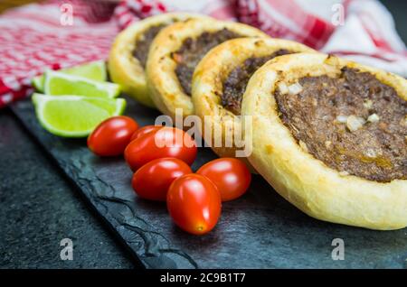 Délicieuse cuisine libanaise (arabe), véritables sfihas sur une plaque d'ardoise avec tomates et citrons à l'arrière-plan avec le keffiyeh libanais traditionnel (turba Banque D'Images
