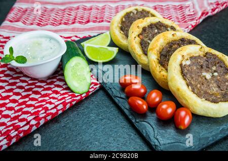 Délicieuse cuisine libanaise (arabe), véritables sfihas sur une plaque d'ardoise avec tomates, citrons et labreh (caillé) à l'arrière-plan avec le traditionnel libanais Banque D'Images