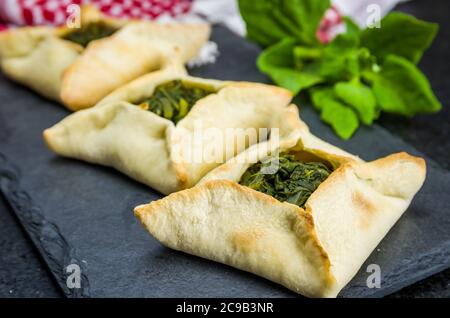 Délicieuse cuisine libanaise (arabe), sfiha aux épinards sur fond de pierre d'ardoise noire et keffiyeh traditionnel libanais de turban. Banque D'Images