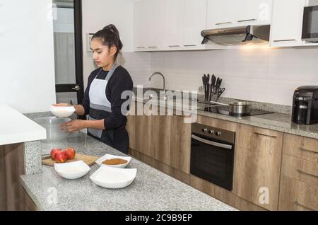 Une adolescente cuisine dans la cuisine de sa maison matériaux pour faire une tarte aux pommes Banque D'Images