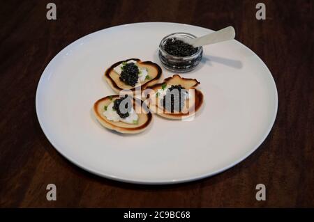 Crêpes russes ou blini à la crème aigre et caviar d'esturgeon noir avec un plein pot de caviar avec une cuillère nacre sur une assiette, gros plan Banque D'Images