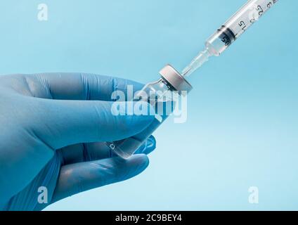 Main du scientifique portant des gants bleus et tenant une ampoule et une seringue. Banque D'Images