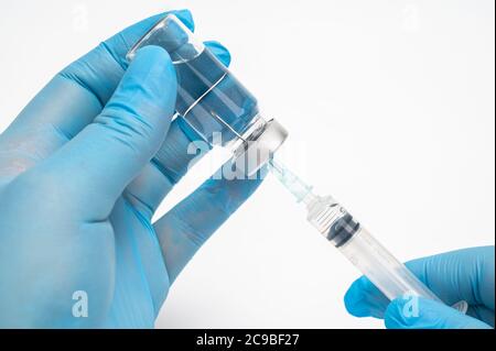 Main du scientifique portant des gants bleus et tenant une ampoule et une seringue. Banque D'Images