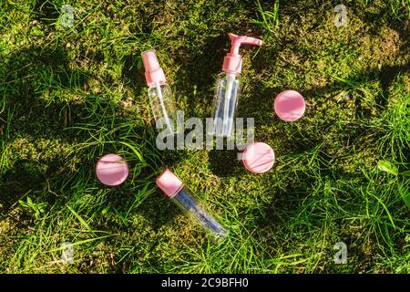 Composition de la couche plate avec des bouteilles en verre rose de cosmétiques biologiques de soin du corps avec de l'huile sur fond de mousse naturelle et d'herbe. Banque D'Images