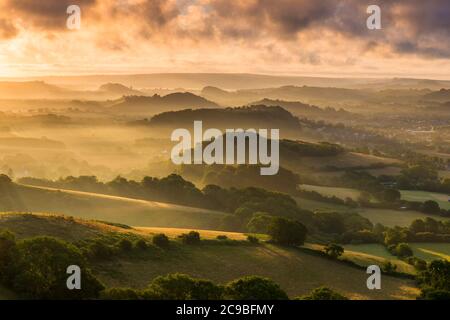 Bridport, Dorset, Royaume-Uni. 30 juillet 2020. Météo Royaume-Uni. Un lever de soleil spectaculaire à Bridport dans Dorset tandis que le soleil levant envoie des rayons du soleil qui brillent à travers les nuages bas à travers les collines à côté de la ville avant un jour d'été chaud prévu. Crédit photo : Graham Hunt/Alamy Live News Banque D'Images