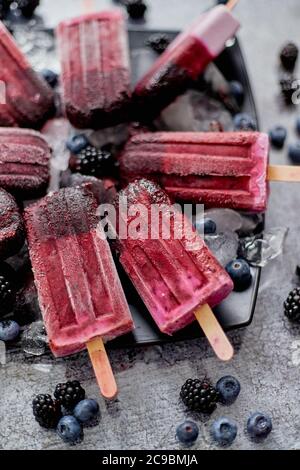 Papsicles faits maison aux myrtilles fraîches et aux mûres sur une assiette noire avec glace sur pierre Banque D'Images