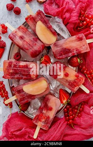 Pop-sicles faits maison à la framboise, à la fraise, aux pommes et au cassis sur une plaque de métal avec baies variées Banque D'Images