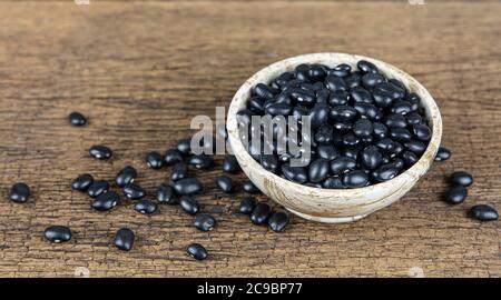 Haricots noirs crus dans un bol en bois sur fond de table en bois. Banque D'Images