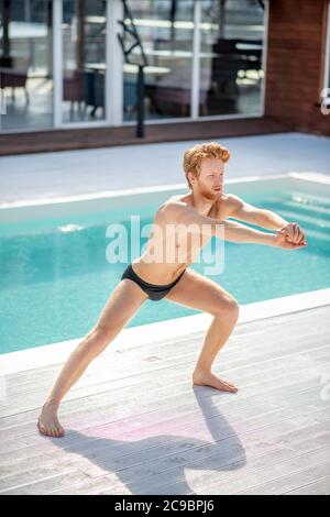 Jeune homme barbu sérieux faisant de l'exercice près de la piscine Banque D'Images