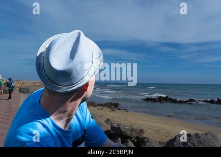 L'homme est assis sur des rochers sur la plage et jouit de la vue. Concept d'été. Banque D'Images