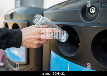 Un homme lance une bouteille en plastique dans un bac de recyclage spécial. Conteneur de tri des déchets Banque D'Images