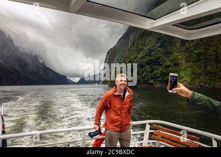 Touriste ayant pris sa photo lors d'une excursion en bateau dans le Milford Sound lors d'une journée de tempête, parc national Fiordland, Southland, Île du Sud, Nouvelle-Zélande Banque D'Images