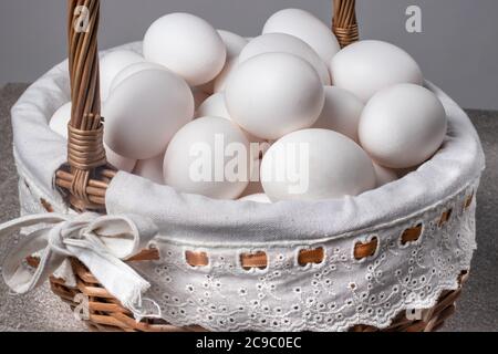Beaucoup d'oeufs blancs de poulet dans un magnifique panier de brindilles en osier. Banque D'Images