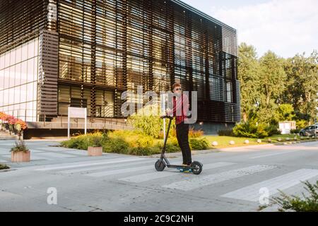 Pleine longueur de beau jeune barbu caucasien sur e le scooter traverse un piéton dans la ville Banque D'Images