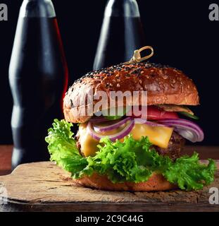 délicieux hamburger avec côtelette de bœuf frite, tomate, laitue et oignons, pain croustillant de farine de blé blanc avec graines de sésame. Restauration rapide sur une planche de bois, behi Banque D'Images