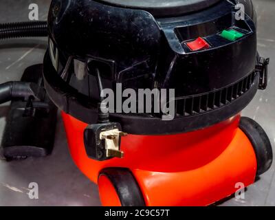 Gros plan d'un ancien aspirateur équipé de roues au sol et d'une fiche britannique accrochée au trou de rangement de câble sur le côté. Banque D'Images